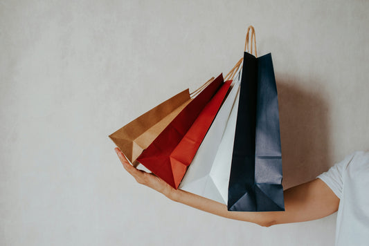 Hand holding colorful shopping bags against a light wall