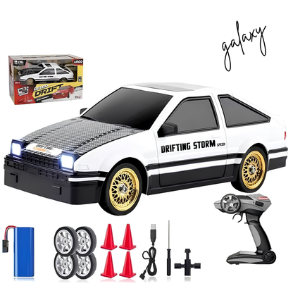 White and black RC drift car with gold wheels, shown with remote control, battery, wheels, cones, and packaging box on a white background. The car has 'DRIFTING STORM' and 'SPEED' decals, and 'galaxy' is written in script.